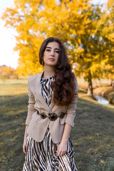 Frontal portrait of a elegant teen girl with make up and hairstyle, dressed in elegant fall outfit, posing in the park.