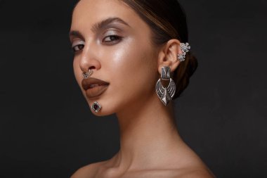 Makyajlı, çıplak omuzlu, siyah arka planda kamera ve takılara bakan bir kızın profil portresini kapat..