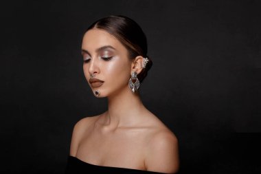Göz kamaştırıcı makyajı ve saçı olan bir kızın profil portresi, stüdyoda çıplak omuzlarla poz vermek, kulakları, boynu, burnu, çenesi, gri arka planı, fotokopi alanı.