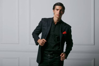 Siyah takım elbiseli, cebinde kırmızı ipek eşarp olan beyaz arka planda kendine güvenen bir gencin ön portresi. Yatay görünüm.