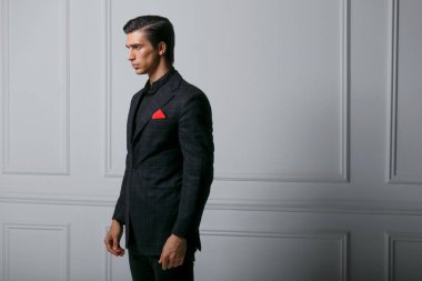 Beyaz arka planda, cebinde kırmızı ipek eşarp olan zarif siyah takım elbiseli kendine güvenen genç bir adam. Yatay görünüm.