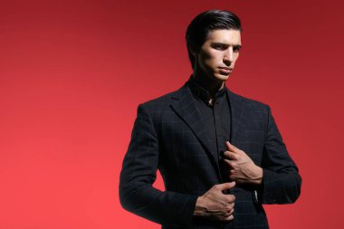 Siyah takım elbiseli, koyu kırmızı arka planda yakışıklı, ciddi bir gencin portresi. Yatay görüş. Metin için boşluk.