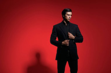 Siyah takım elbiseli, koyu kırmızı arka planda yakışıklı, ciddi bir adamın ön portresi. Yatay görüş. Metin için boşluk.