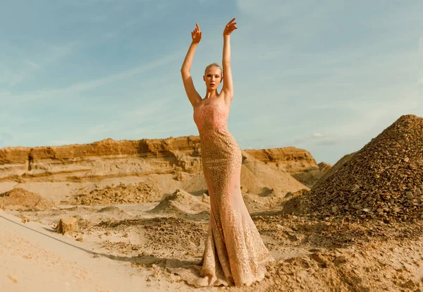 Full length image of a gorgeous lady in slim beautiful dress posing in desert at the sunset. Frontal portrait.