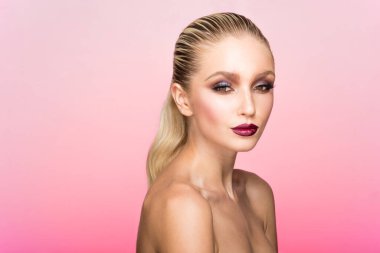 Mükemmel makyajlı ve saçı düzleştirilmiş ve açık pembe arka planda kalmış genç bir kadının profil portresi..