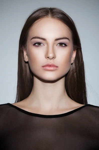 Closeup frontal portrait of a attractive young woman of make-up, wear in black dress, looking at camera, over grey background.