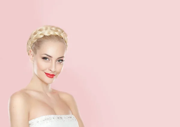 Frontal portrait of a cheerful blonde young woman with bright make-up and hairstyle, with bare schoulders, over pink background. Space for text.