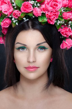 Siyah arka planda, makyajlı, pembe çiçekli güzel esmer bir kadının yakın plan portresi..