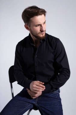 Beyaz arka planda oturan sakallı bir gencin yakın plan portresi..