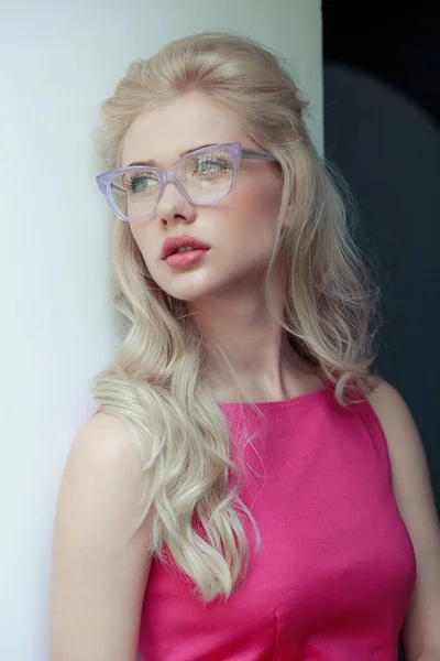 Close up frontal portrait of a beautiful blonde woman with makeup wearing stylish eyeglasses, looking a side.