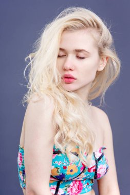 Gri arkaplan üzerinde, gözleri kapalı ve omuzları çıplak poz veren güzel sarışın bir kadının ön portresi..