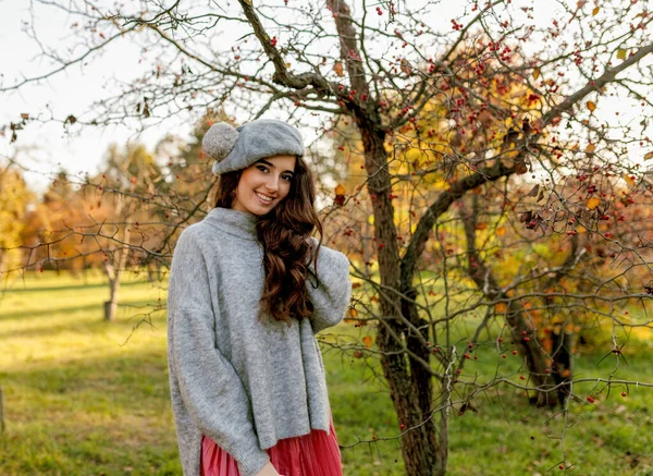 Smiling brunette girl in fall outfit and beret stands among yellow trees in the park. — Stock Photo, Image