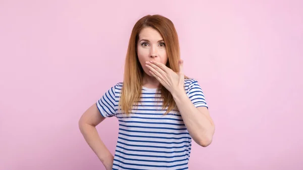 Silencio. Mujer asustada cubriendo la boca con las manos mientras posando a la cámara en el fondo del estudio rosa. Chica sorprendida cerrar los labios con las palmas de las manos, no hablan mal concepto . — Foto de Stock