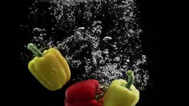黒の背景に水と回転する空気の泡に落ちる赤と黄色のピーマン — ストック動画