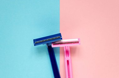 Üst görünümde iki yeni tek kullanımlık tıraş bıçağı mavi-pembe arka planda fotokopi alanı ile yan yana duruyor. Minimum şey. Erkek-kadın ilişkisi kavramı. Asgari düşünce