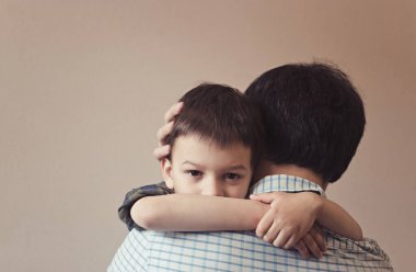 Üzgün oğul, arka planda bej duvarlı fotokopi aletiyle babasına sarılıyor. Baba-oğul ilişkisi kavramı