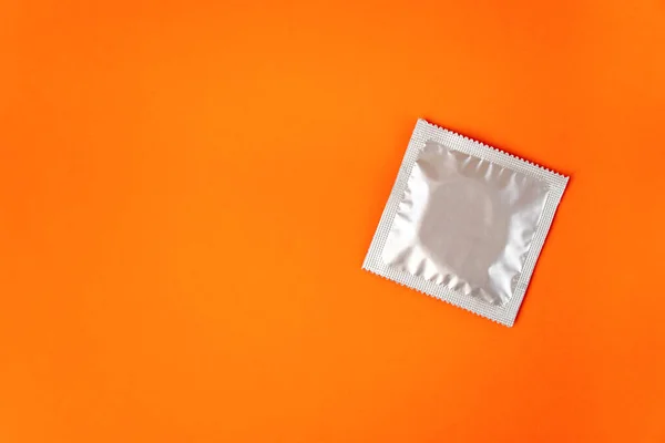 Üst görünüm, turuncu arkaplanda izole edilmiş gümüş renkli bir prezervatif.