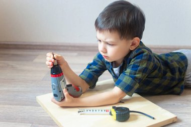 Çocuk yerde yatıyor ve elinde tornavidayla inşaat ruletinin yanında duruyor. Çocuk inşaat araçlarıyla oynuyor