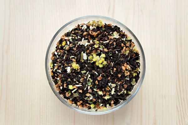 Ahşap arka planda izole edilmiş yuvarlak kâse içinde Aromatik kuru çiçek çayı yaprakları. Üst manzara, siyah çiçek çayı.