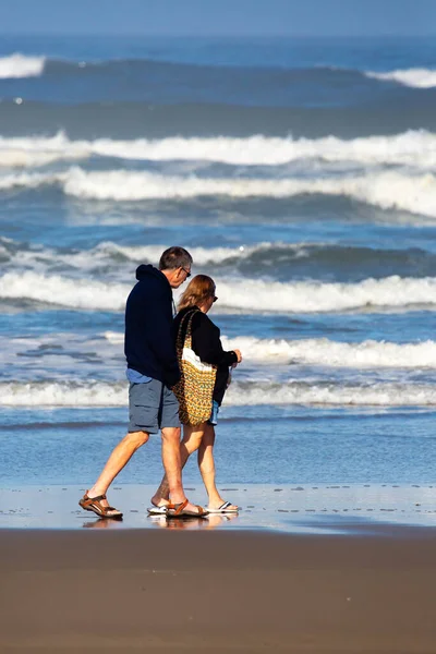 Pasifik Okyanusu kıyısında sahilde yürüyen yaşlı çift, dikey.