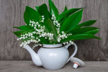 Vadinin zambakları beyaz bir çaydanlıkta duruyor. Ahşap bir arka planda, ön tarafta.