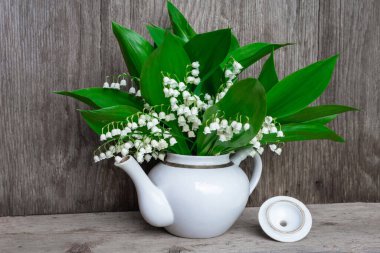 Vadinin zambakları beyaz bir çaydanlıkta duruyor. Ahşap bir arka planda, ön tarafta.