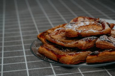 Elmalı, tarçınlı ve pudra şekerli pudra pudralı börekler masanın üzerinde kareli masa örtüsüyle.