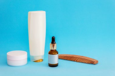 Mavi arka planda pipetli bir kavanoz ve boş bir çıkartma var. Yuvarlak beyaz bir kavanoz, ahşap tarak, büyük beyaz bir şişe.