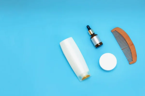 Mavi arka planda pipetli bir kavanoz ve boş bir çıkartma var, yuvarlak beyaz bir kavanoz, ahşap tarak, büyük beyaz bir şişe, üst taraftan manzara.
