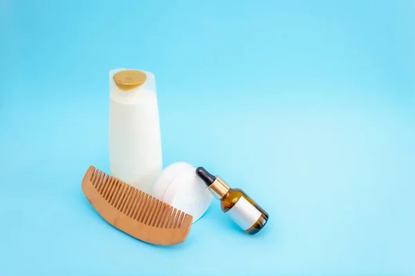 Mavi arka planda pipetli bir kavanoz ve boş bir çıkartma var. Yuvarlak beyaz bir kavanoz, ahşap tarak, büyük beyaz bir şişe.