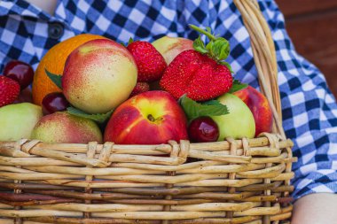 Kızın elleri sepetin içinde duran nektarin, portakal, çilek, kiraz ve nane yapraklarını tutuyor. tahta arkaplan