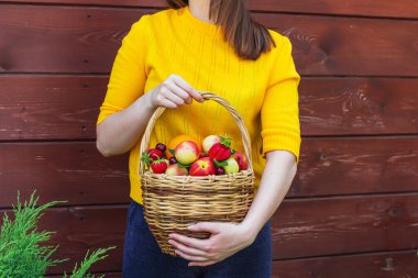Tahta bir duvarın arkasında duran esmer genç bir kız tarafından taze meyveyle dolu sepet tutulur.