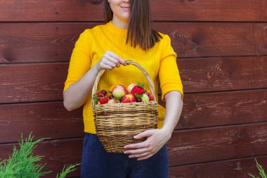 Tahta bir duvarın arkasında duran esmer genç bir kız tarafından taze meyveyle dolu sepet tutulur.