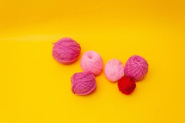 Sarı arka planda eflatun ve pembe renkli yün iplikler var.