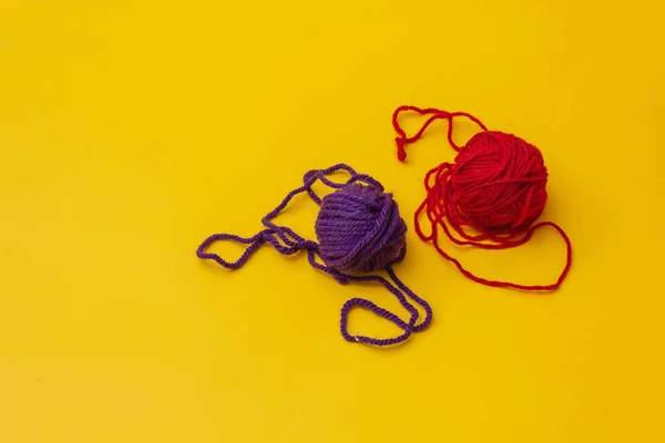 a tangles of red and blue woolen threads lies unraveled on a yellow background. the view from the top