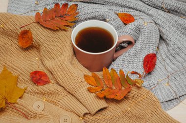 Sonbahar, kuru kırmızı sonbahar yaprakları sıcak bir espresso bardağının etrafına istiflenmiş süveterlerin üzerinde yatar.