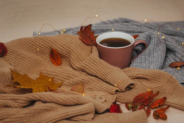 Autumn, dry red autumn leaves lie on sweaters that are stacked around a hot espresso mug, around lies a led garland, Flatley — Stock Photo, Image