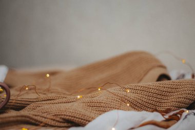 Masanın üzerinde bej renkli yün örgü bir kazak ve açık kahverengi bir pamuk atkı var. Tepede bir çelenk var. yan görünüm