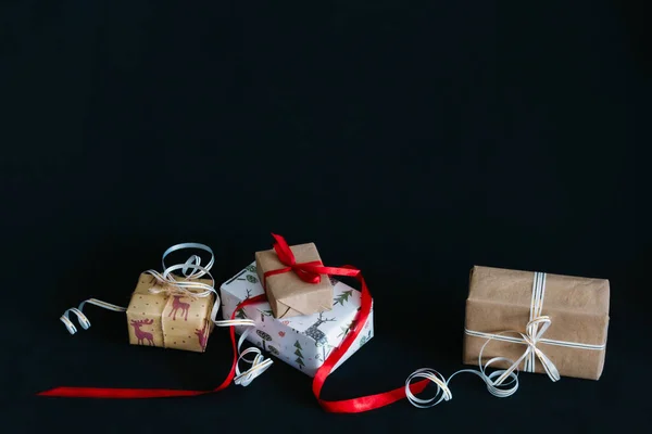 Caixas de presente Embalado em papel de embrulho e amarrado com fitas para o ano novo ou Natal mentira em uma pilha em um fundo preto — Fotografia de Stock