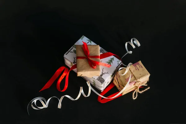 在黑色的背景上 是用包装纸包着 用缎带捆着的圣诞礼物 一个用红色缎带捆着的小木箱 一个用金色缎带捆着的大盒子 — 图库照片