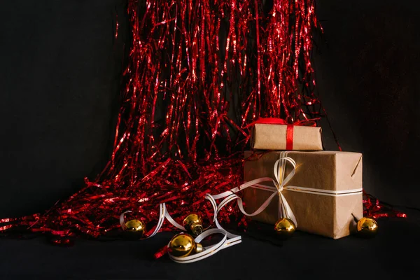 クリスマスプレゼントはティンセルの黒い背景にあり その隣にはゴールデンクリスマスツリーのおもちゃのボールがあります クリスマスのプレゼントを用意するというコンセプト — ストック写真