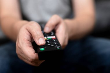 El, kanalı seçmek için uzaktan kumandaya basıyor. Boş zamanlarınızı evde film izleyerek geçirin..