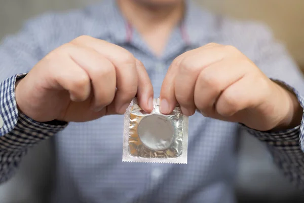 Prezervatifi elinde tutan bir adam. Güvenli seks hayatı kavramı. Enfeksiyonu, doğum kontrolünü, doğum kontrolünü önle. Sağlık ve sağlık hizmetleri.