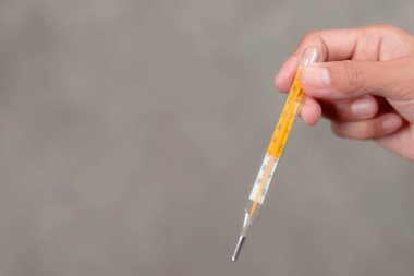 Bir kadının eli termometreyi tutuyor..