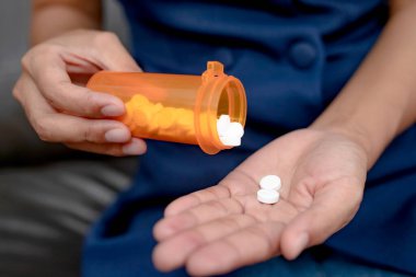 Çalışan kadın haplarını içerken, ağrı kesicileri, sağlık hizmetlerini ve ilaç konseptini azaltmak için ağrı kesicileri içerek şişeden boşaltıyor..