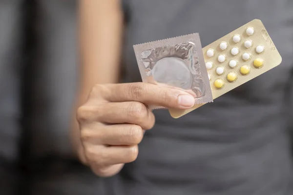 Woman hand holding contraceptive pills and condom sitting on sofa background,protection, safe sex,contraceptive means.