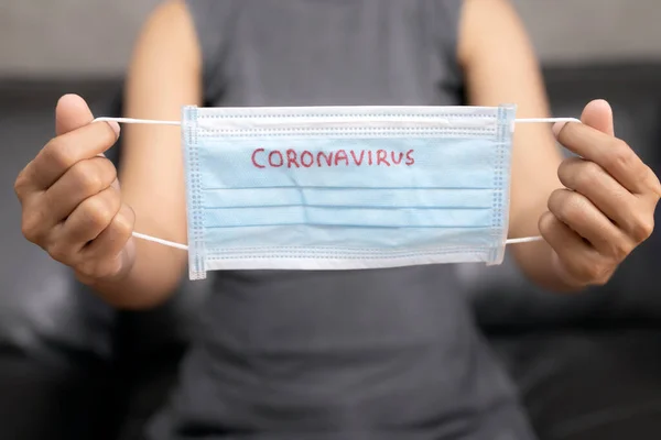 Kadının eli grip hastalıklarına karşı korunmak için bir maske tutuyor. Korunmak için koruyucu maske takan kadın, diğerlerinin COVID-19 ve SARS COV 2 enfeksiyonlarından korunmak için evden çalışıyor..