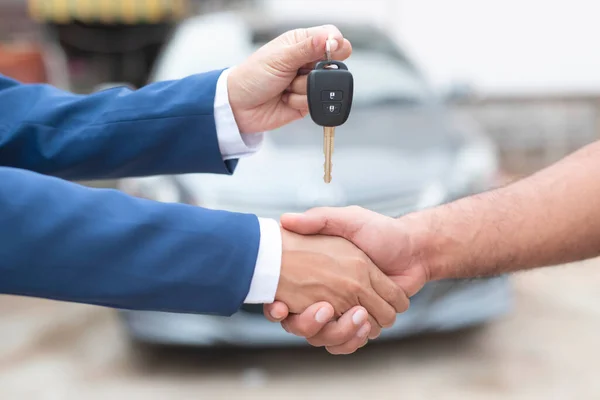 Close up of dealer giving key to new owner and shaking hands in auto show.auto business, car sale, deal,concept