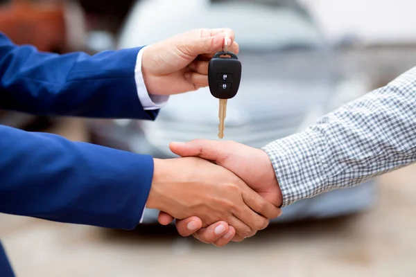 Close up of dealer giving key to new owner and shaking hands in auto show.auto business, car sale, deal,concept