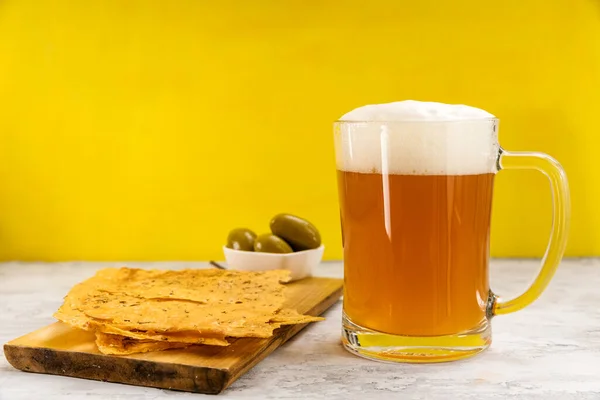 A mug of foamy beer with delicious focaccio tortillas and green olives.